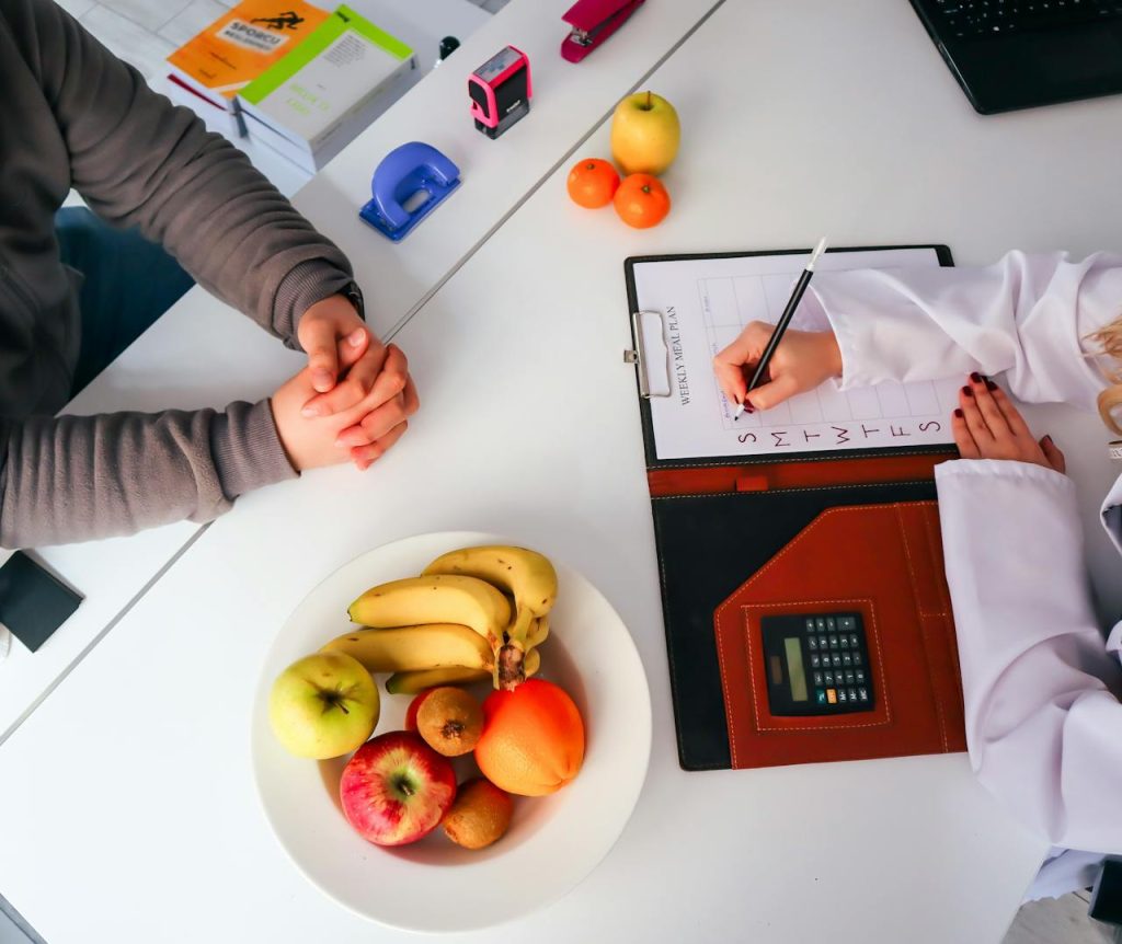 Vue de dessus d'une diététicienne en train d'élaborer un régime alimentaire équilibré, avec des fruits frais sur la table, en mettant l'accent sur la santé et la nutrition.