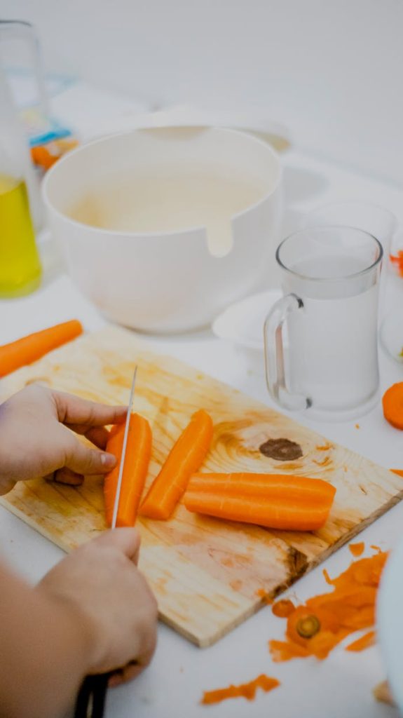 Gros plan sur des mains en train de couper des carottes d'un orange vif sur une planche à découper en bois, dans une cuisine.